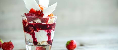 A clear glass containing a layered dessert with strawberries and cream.