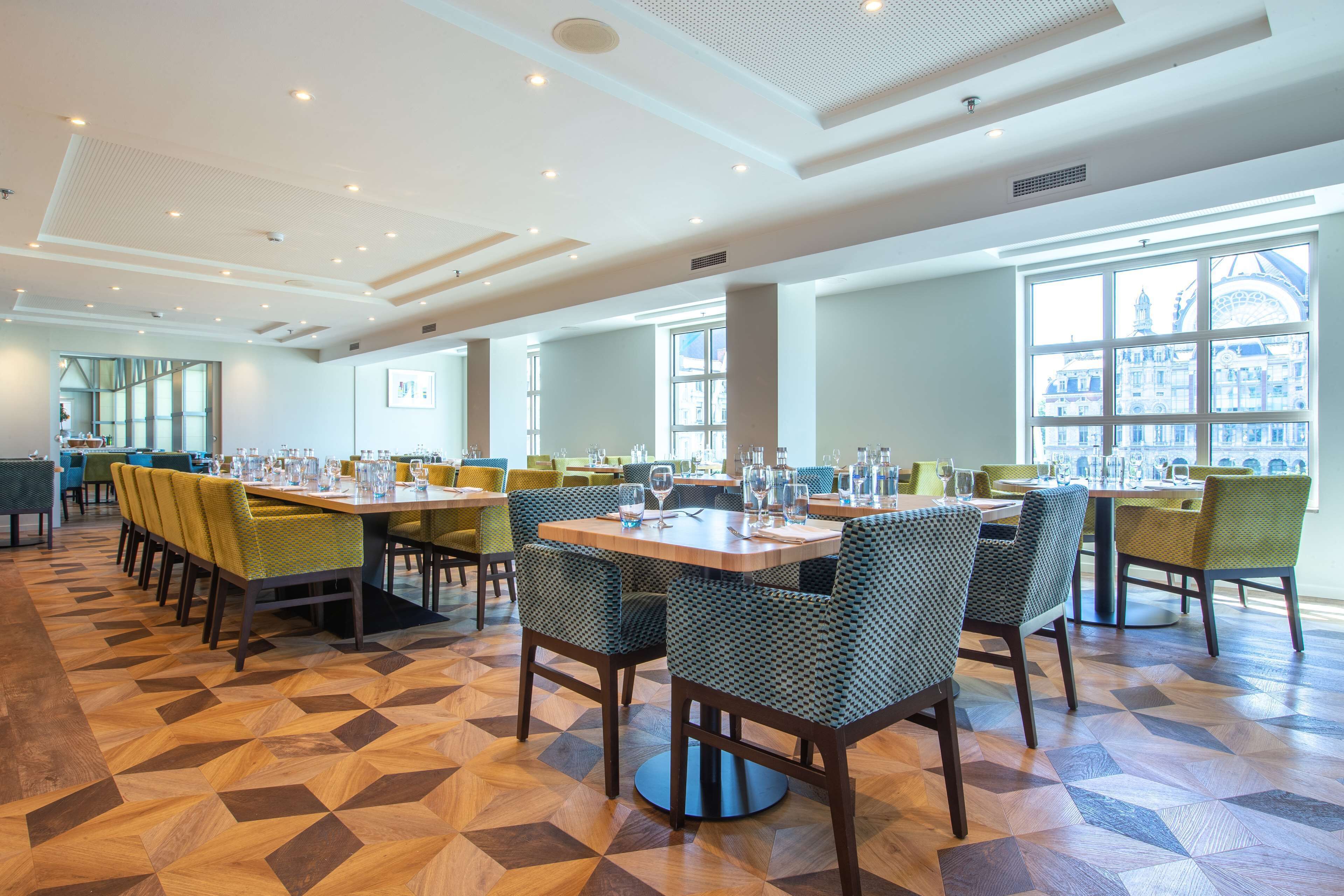 A spacious dining area with multiple tables and chairs, large windows with a view of a historic building, and a patterned floor.