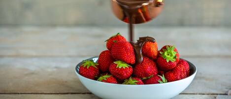 A bowl of strawberries with syrup being poured over them.