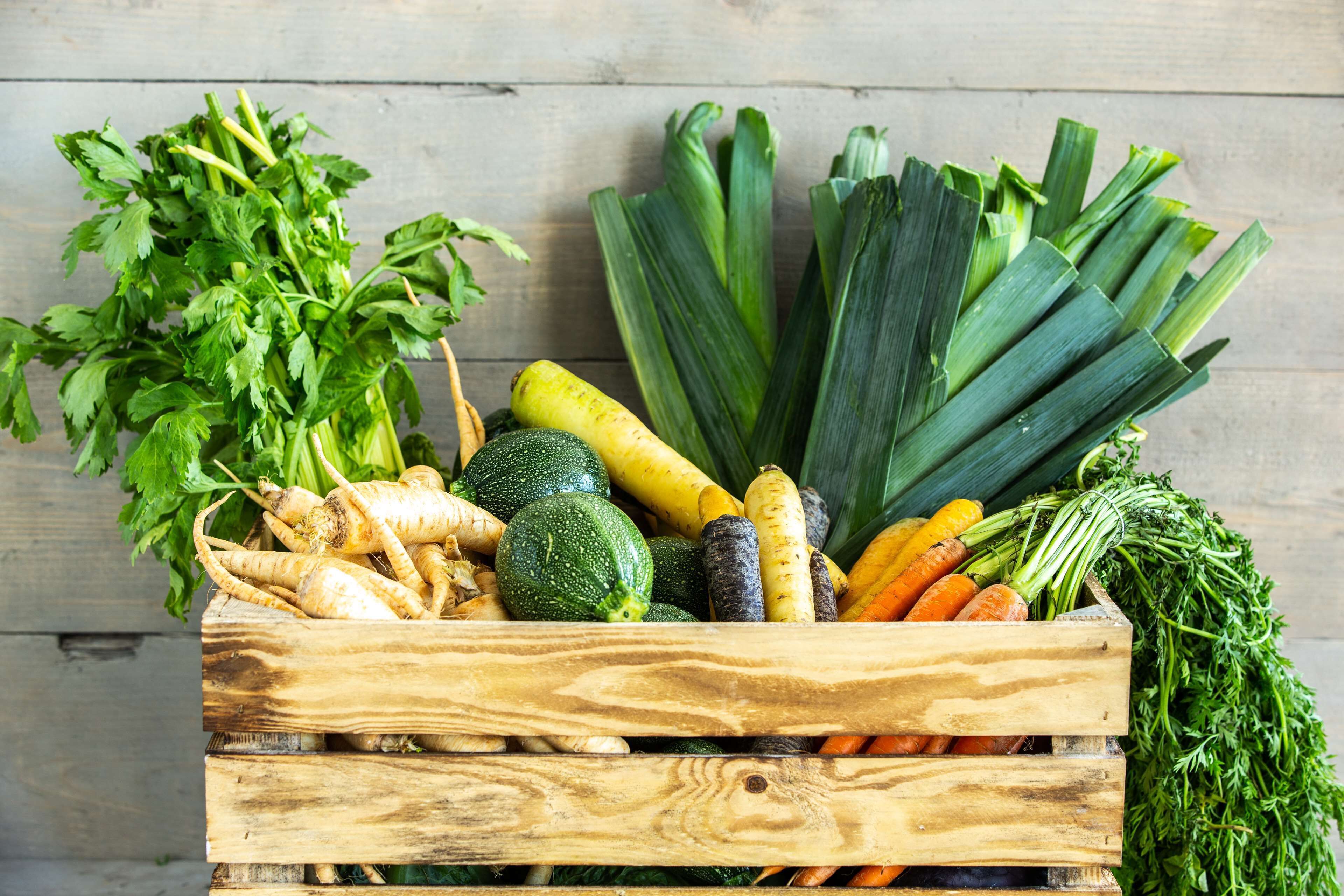 Une caisse en bois remplie de divers légumes, notamment des légumes-feuilles, des carottes et des courges.