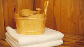 A wooden tub with a wooden scoop and ladle, placed on a stack of white towels against a wooden wall.