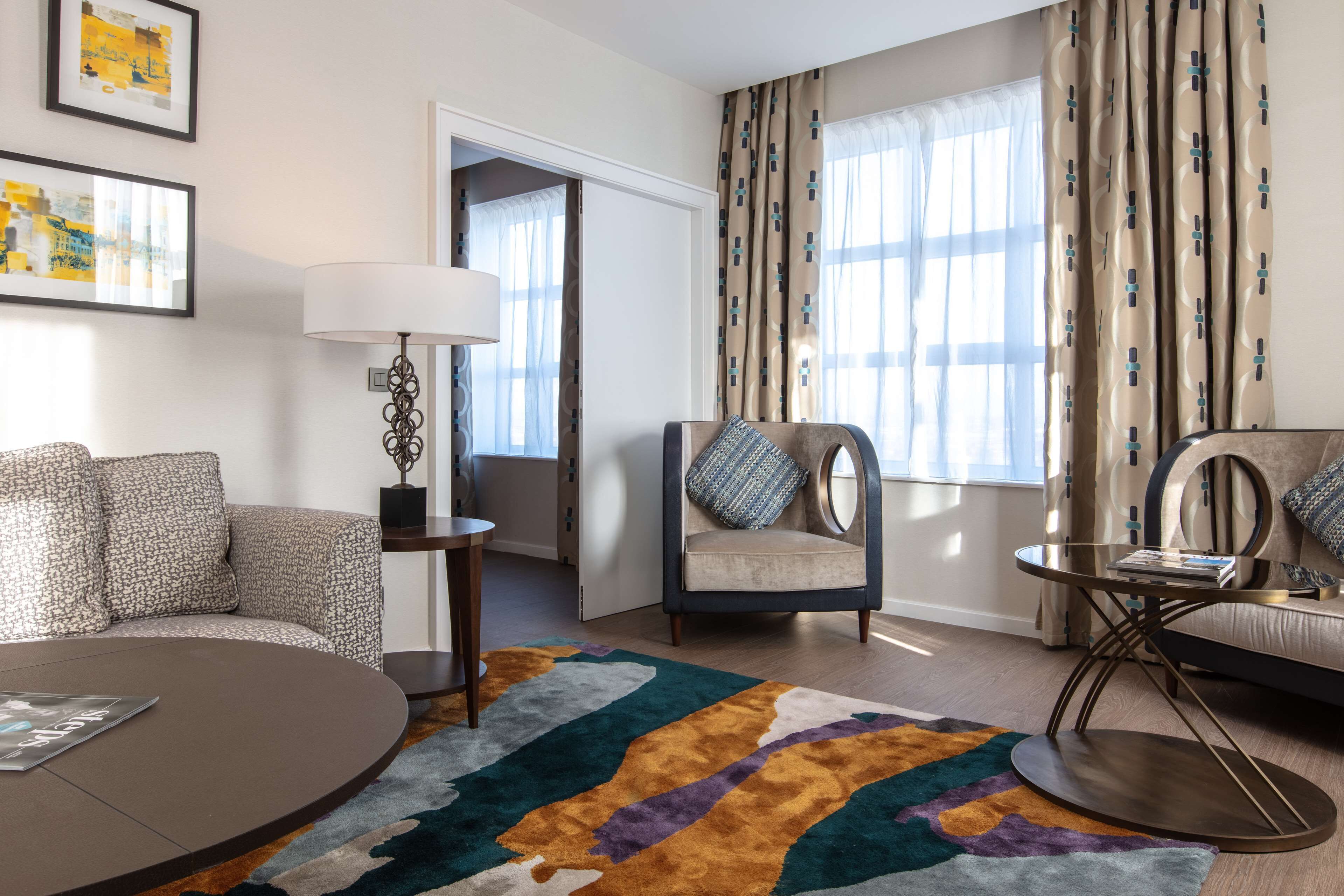 Ein modernes Hotelzimmer mit einer Couch, einem Sessel und einem runden Couchtisch.