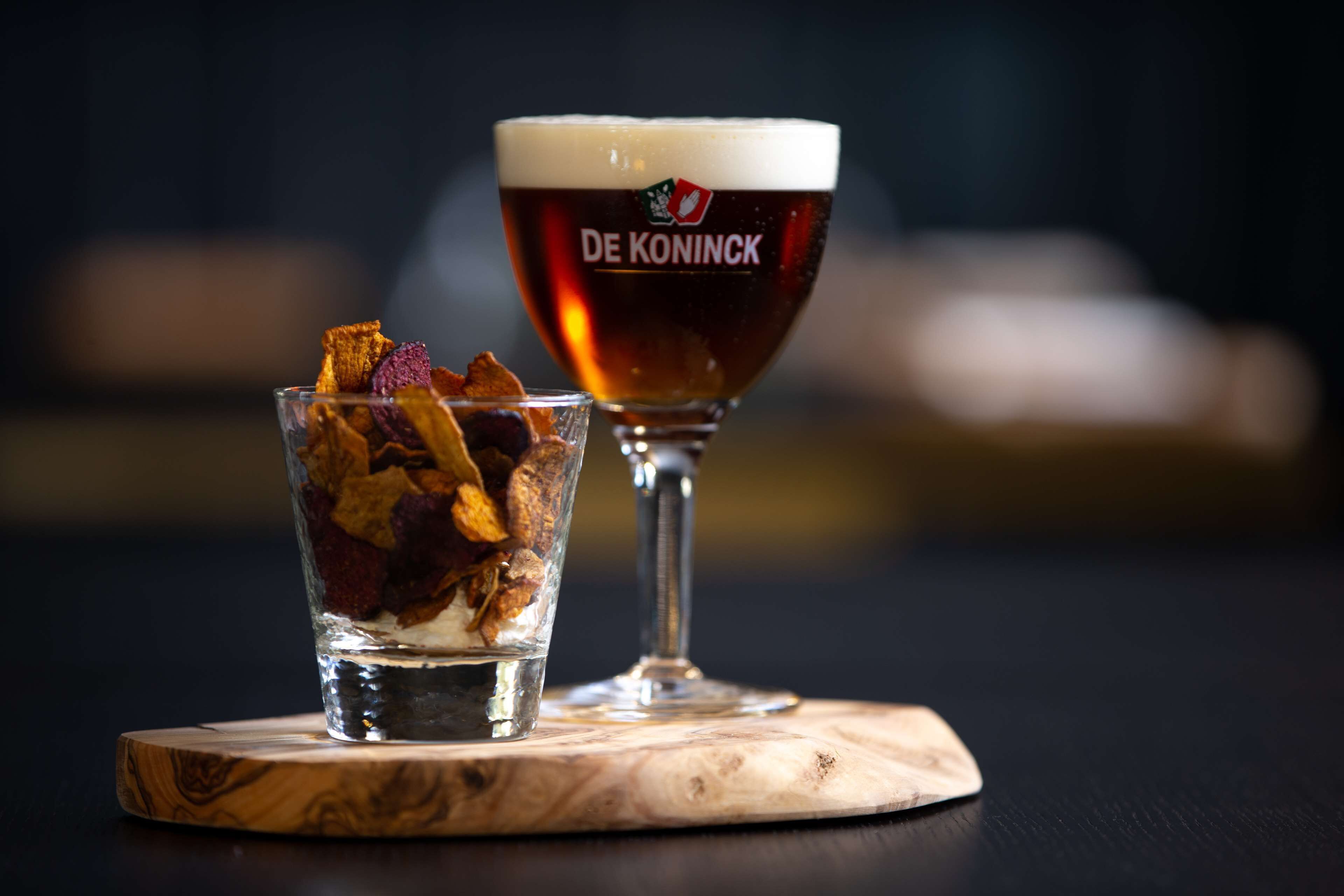 A glass of beer with a logo and a glass of water with dried fruit on a wooden coaster.