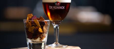 A glass of beer with a logo and a glass of water with dried fruit on a wooden coaster.
