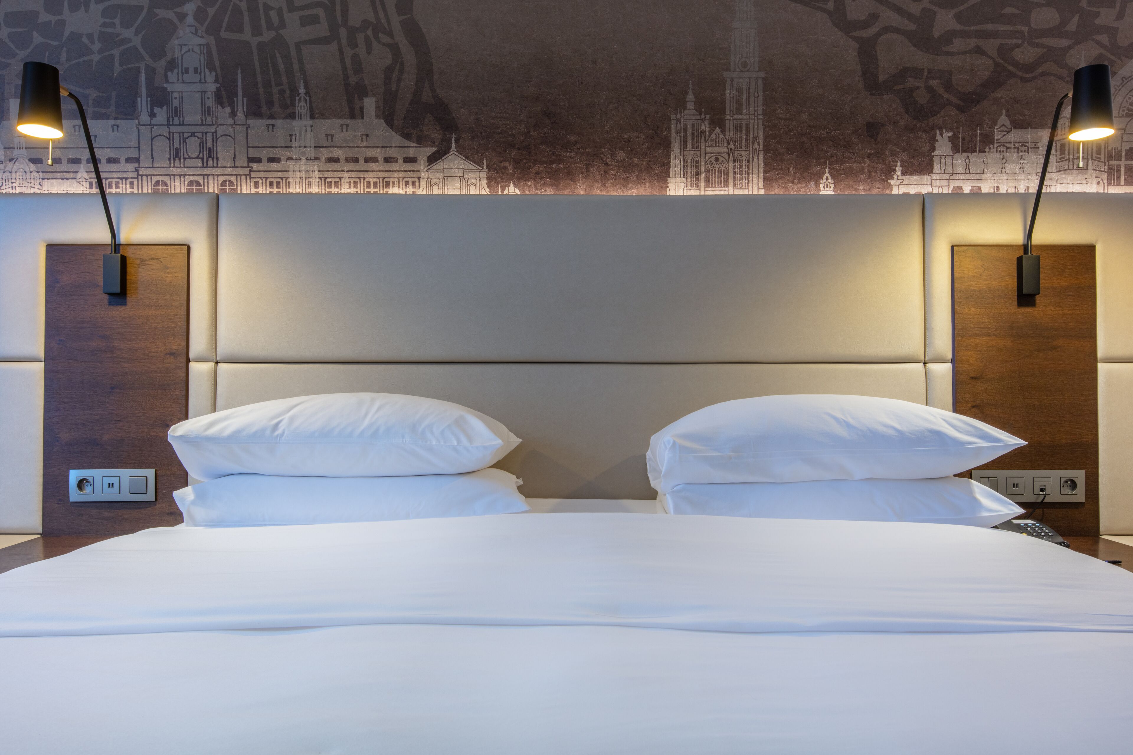 A hotel room with a large bed, two bedside lamps, and a wall mural.