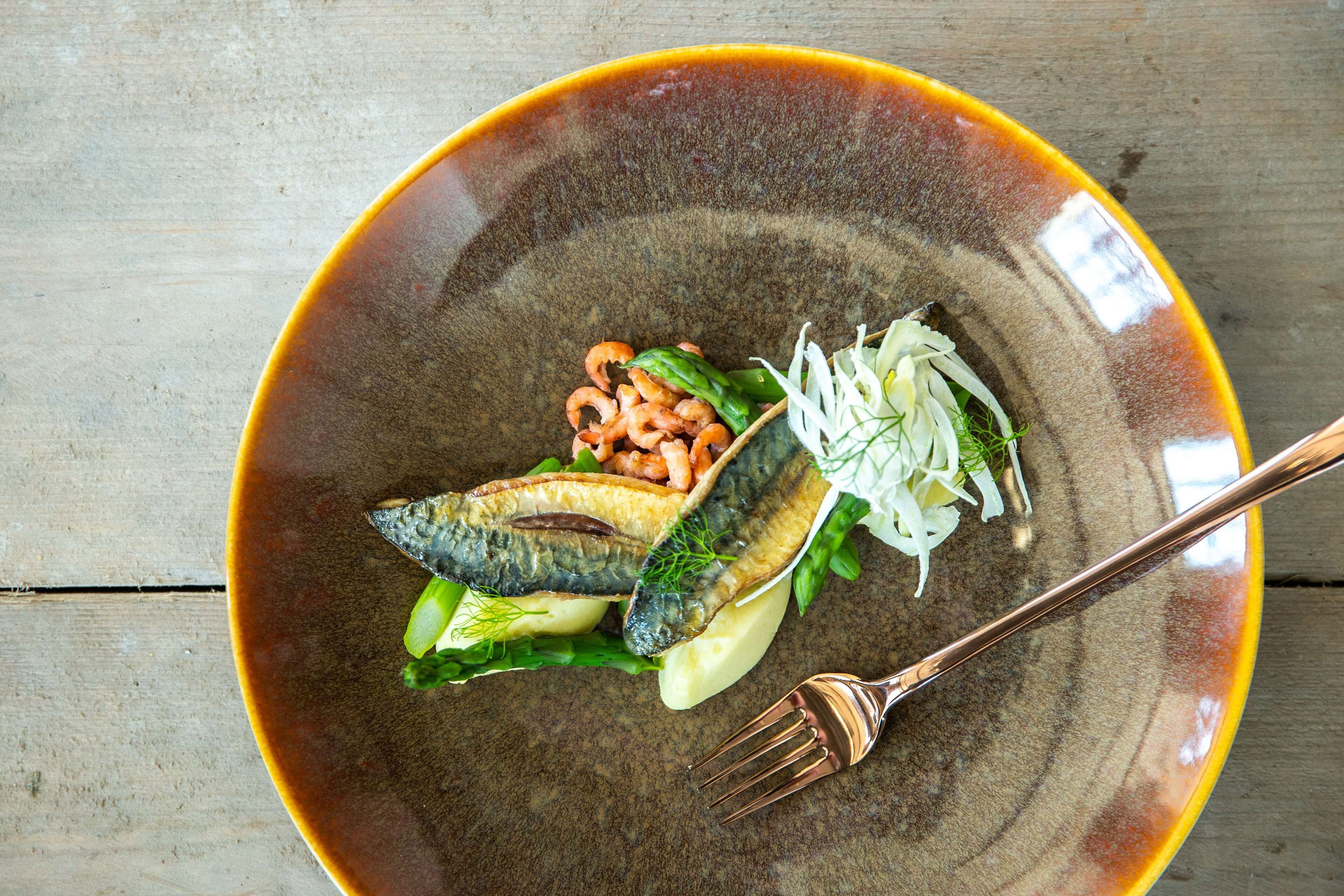 Un plato con pescado, verduras y un tenedor sobre una mesa de madera.