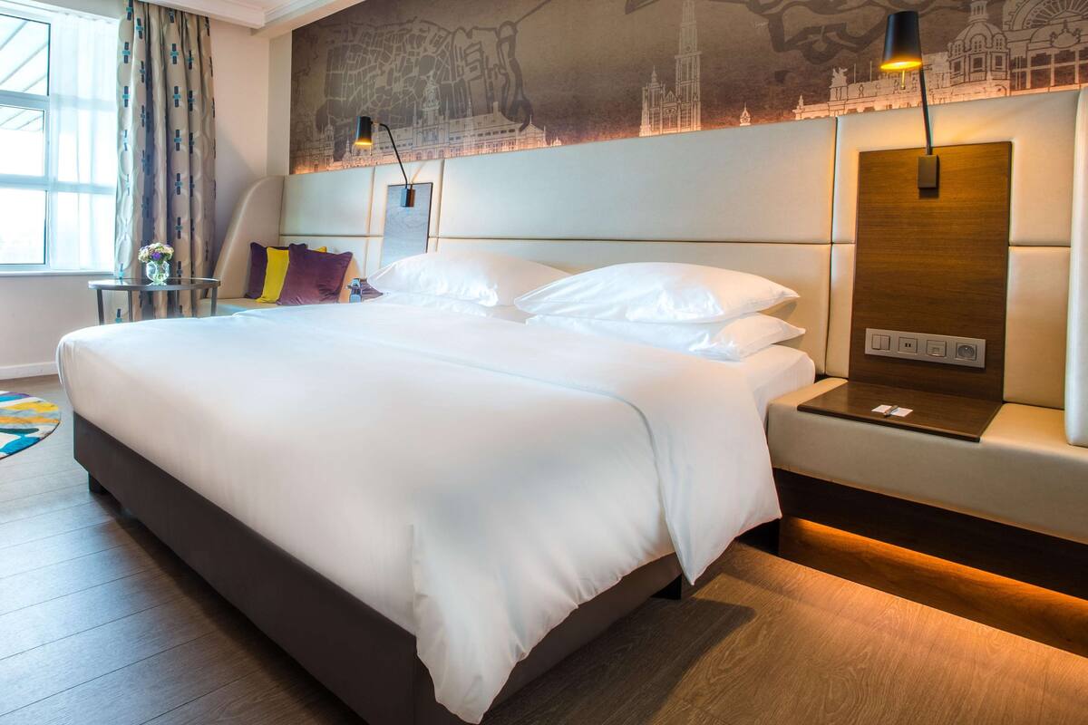 Una habitación de hotel moderna con una cama grande, una mesita de noche, una lámpara y un panel de control en la pared.