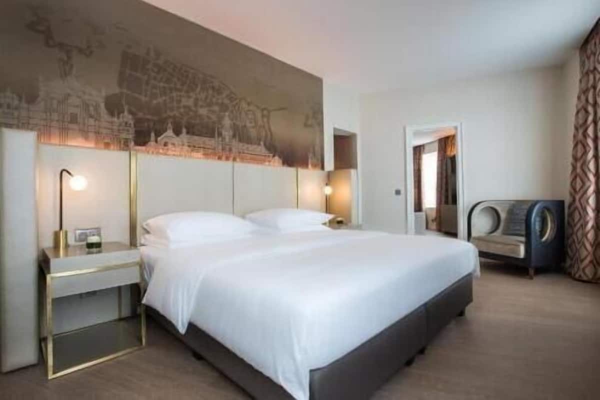 Habitación de hotel con una cama grande, mesitas de noche, una obra de arte colgada en la pared y un rincón de descanso con una silla.