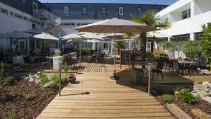 A wooden deck with outdoor seating, umbrellas, and a signboard. - ibis Styles Poitiers Nord (Poitiers)