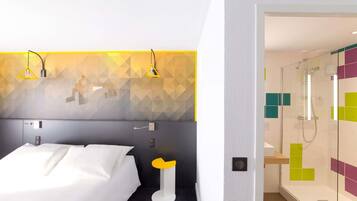 A hotel room with a bed, a bedside table, a shower area, and a wall with geometric patterns.
