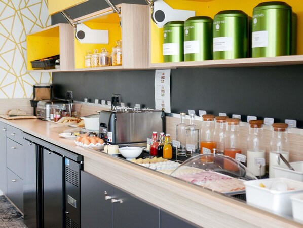 A breakfast buffet with various food items, condiments, and green canisters on shelves.