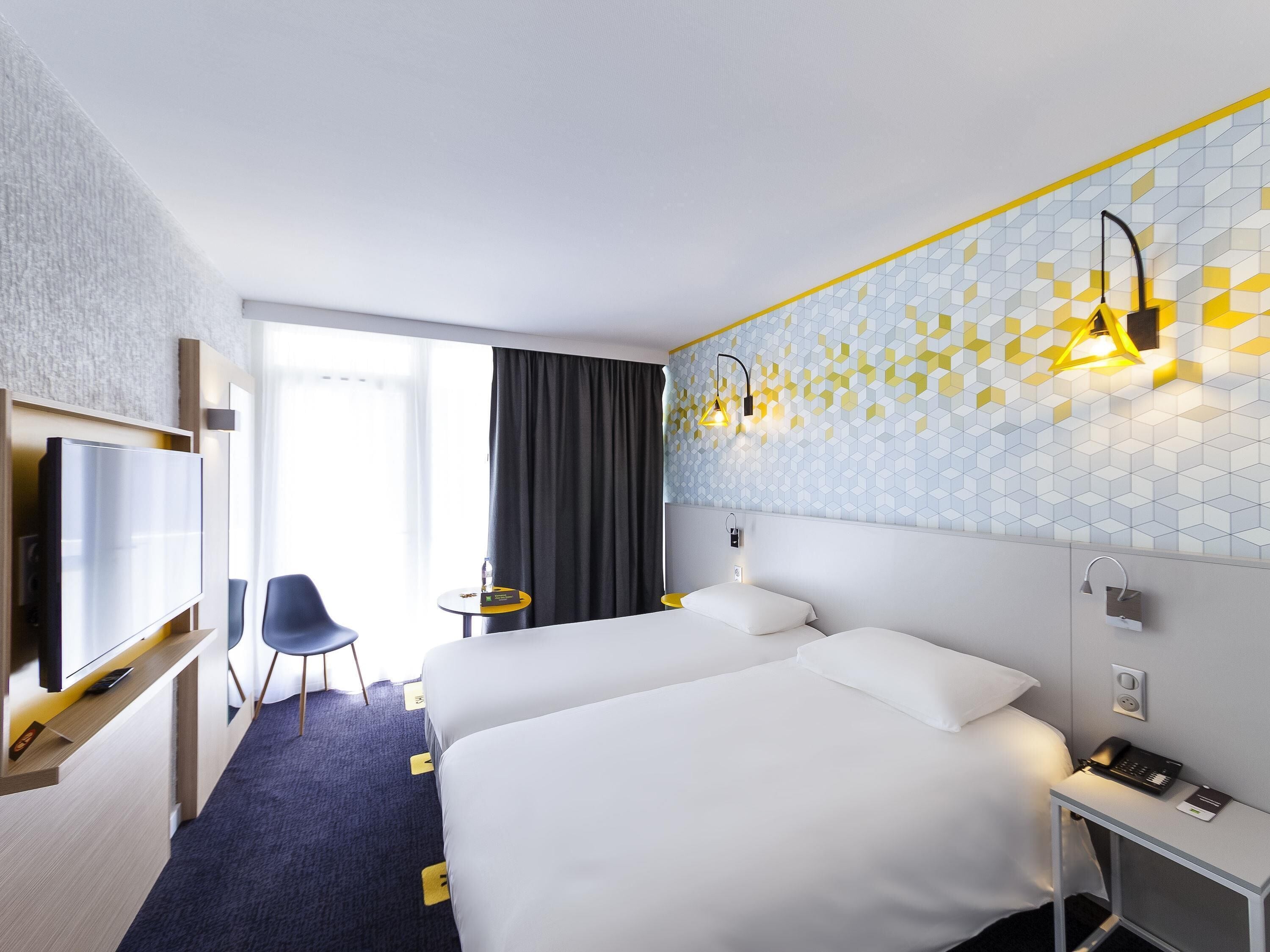 A hotel room with two beds, a TV, a desk, and a chair.