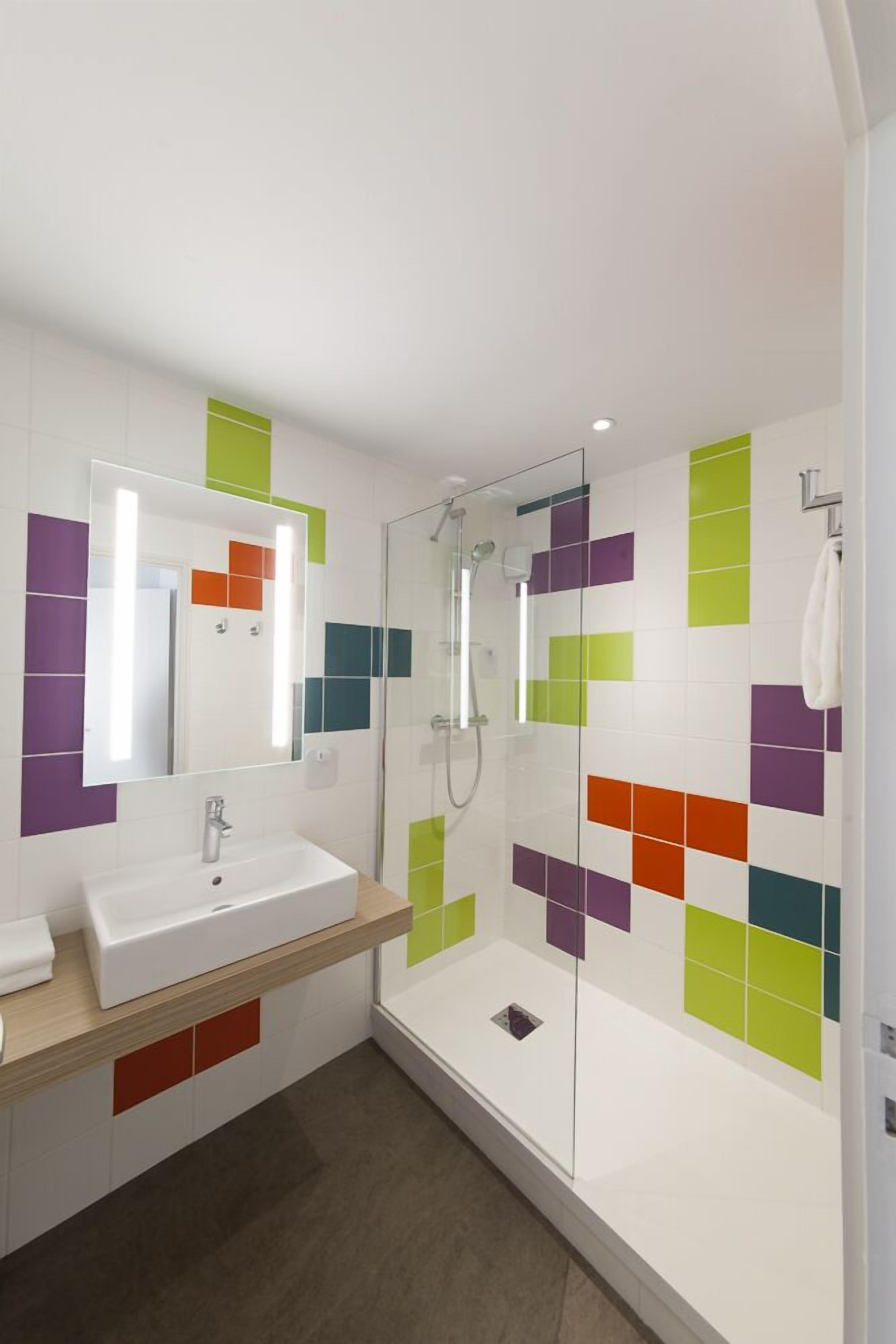 Une salle de bain moderne avec un lavabo blanc, une douche en verre et des carreaux colorés sur les murs.