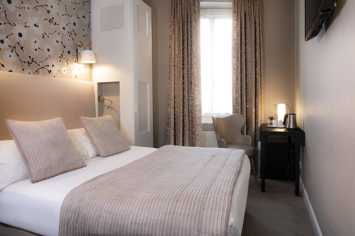 Une chambre d’hôtel avec un grand lit, un bureau, une chaise et une fenêtre avec des rideaux.