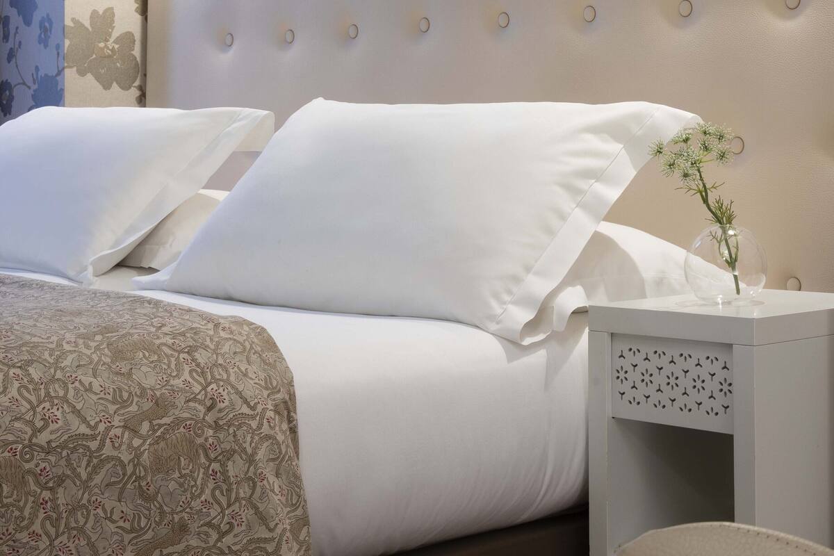 Un lit bien fait, avec des draps blancs et une couvre-lit à motifs floraux.