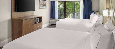 A hotel room with two beds, a flat-screen TV mounted on the wall, a small kitchenette, and a large window with curtains.