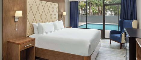 Ein Hotelzimmer mit einem großen Bett, einem Schreibtisch, einem Stuhl und Blick auf einen Swimmingpool.