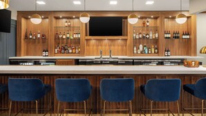 Un espace bar avec des étagères en bois, un grand téléviseur et des tabourets de bar.