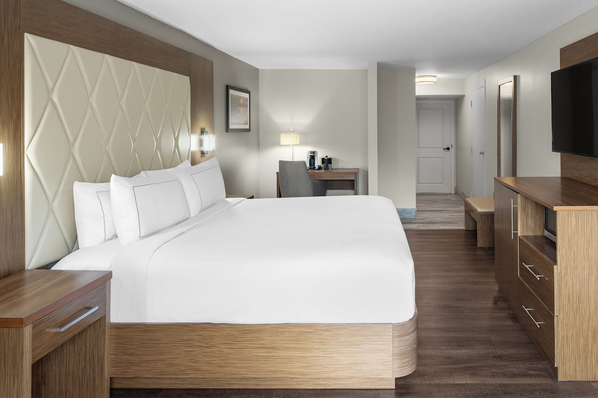 Een moderne hotelkamer met een groot bed, een houten hoofdeinde, nachtkastjes, een bureau met een stoel, een televisie en een deur die naar een andere kamer leidt.