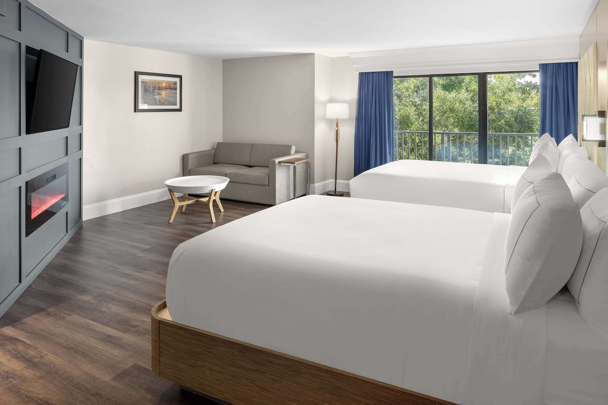 Een hotelkamer met een groot bed, een kleiner bed, een slaapbank, een televisie en een raam met gordijnen.