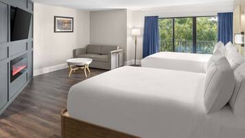 Habitación de hotel con una cama grande, una cama más pequeña, un sofá, un televisor y una ventana con cortinas.