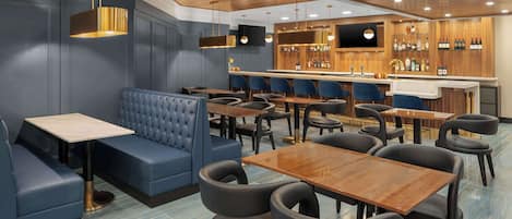 A restaurant with blue booths, wooden tables, and a bar area with shelves of bottles.