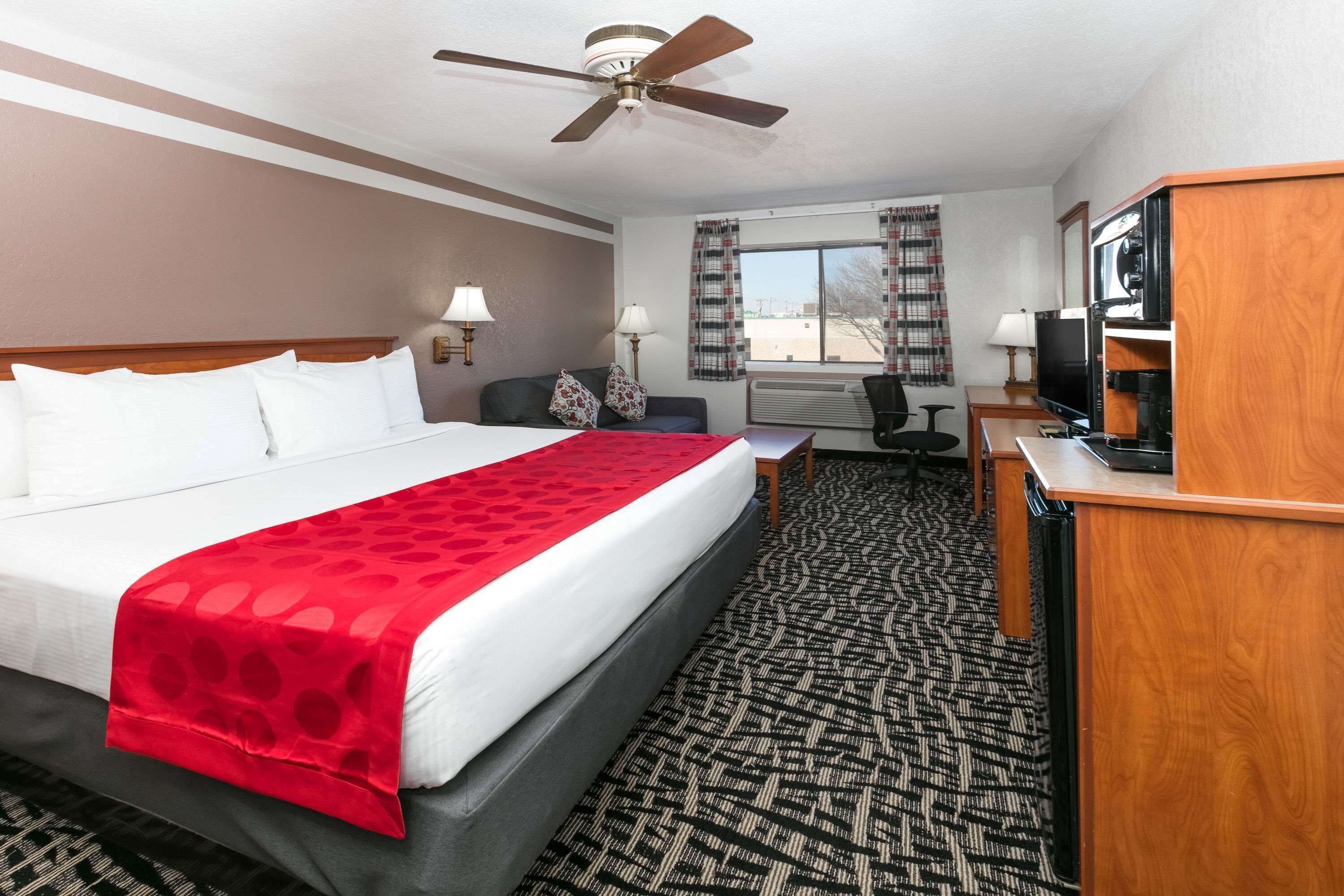 A hotel room with a large bed, a desk with a television, a ceiling fan, and a window with curtains.
