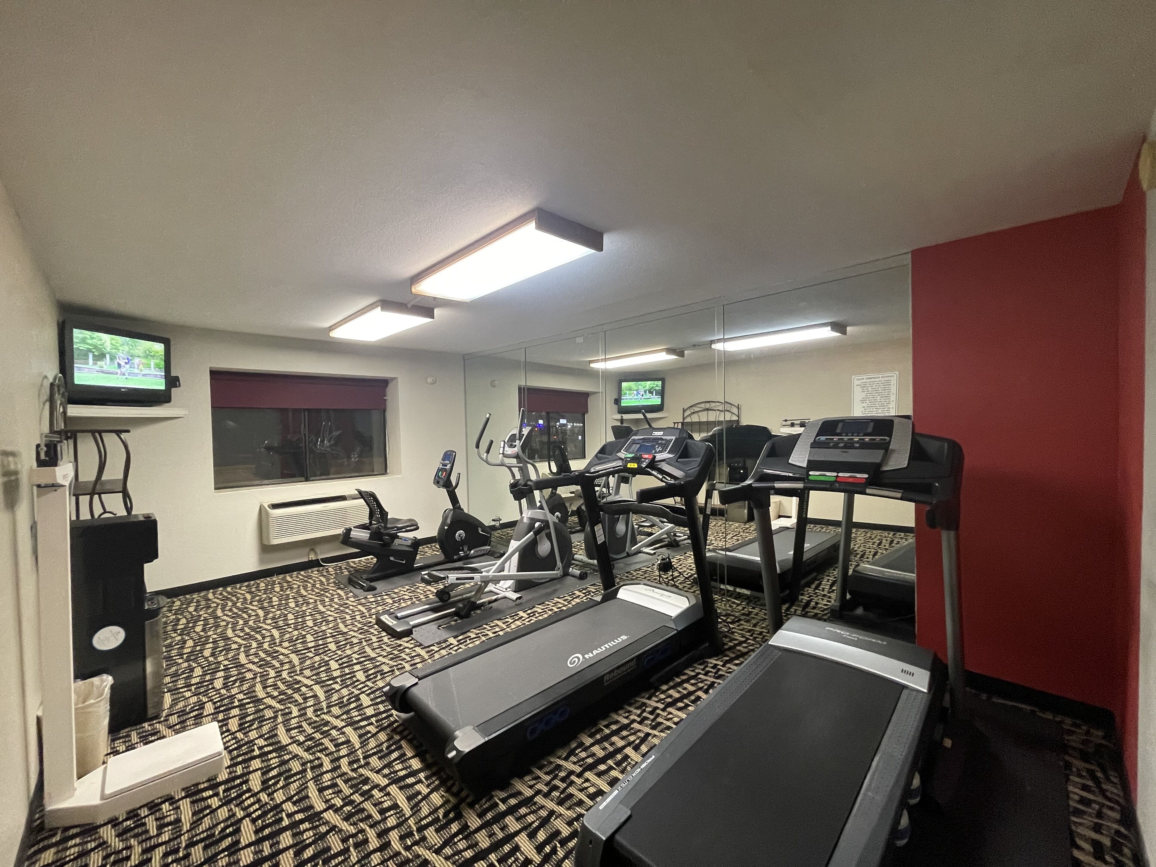 A hotel gym with treadmills, elliptical machines, and a mirrored wall.