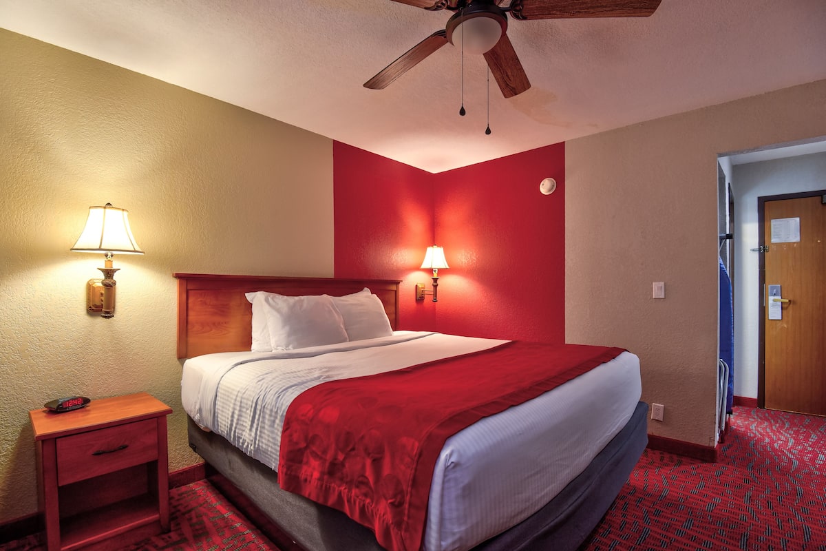 A hotel room with a bed, two bedside lamps, a nightstand, a ceiling fan, and a door.