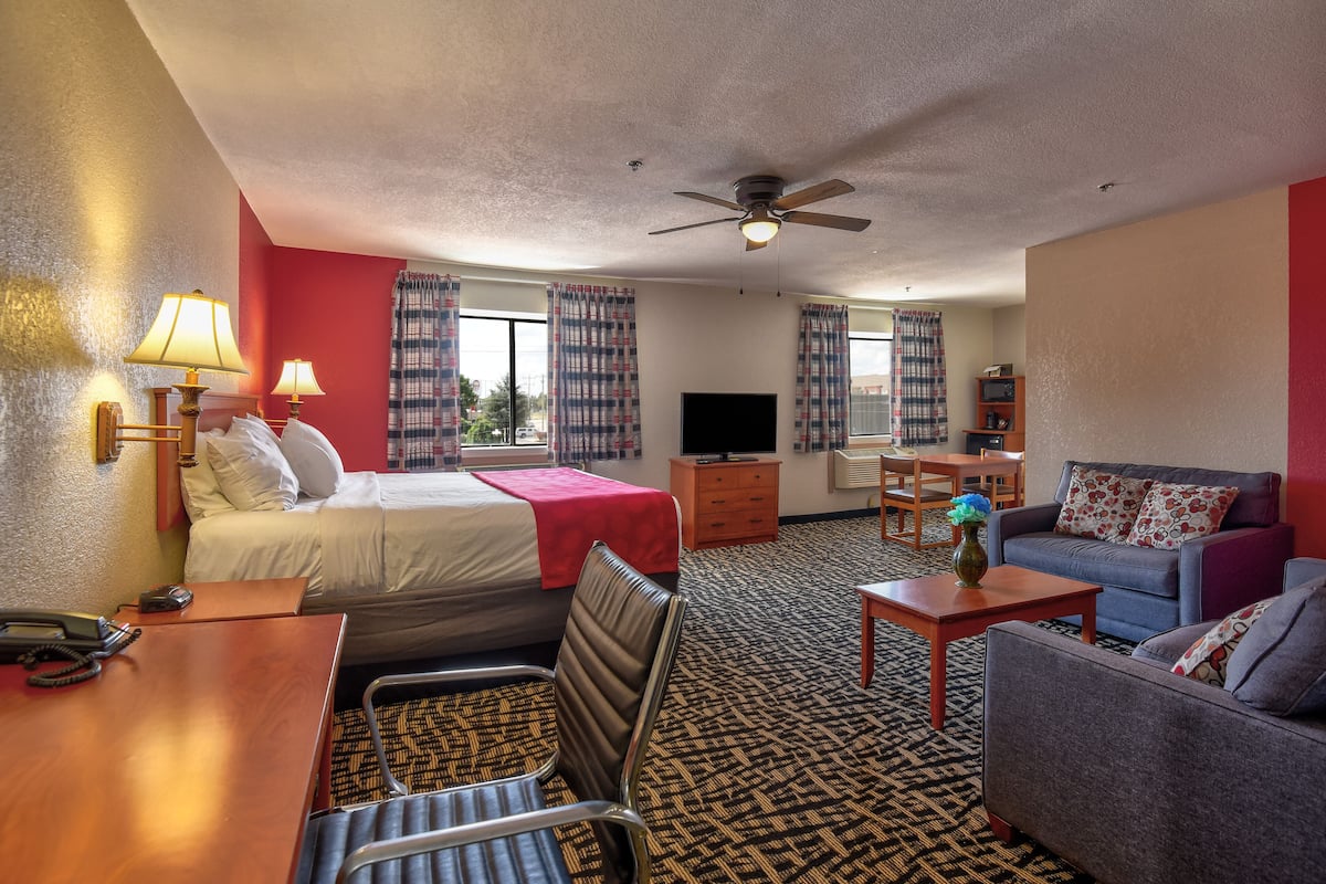 A hotel room with a bed, a sofa, a desk with a lamp, a television, and a ceiling fan.