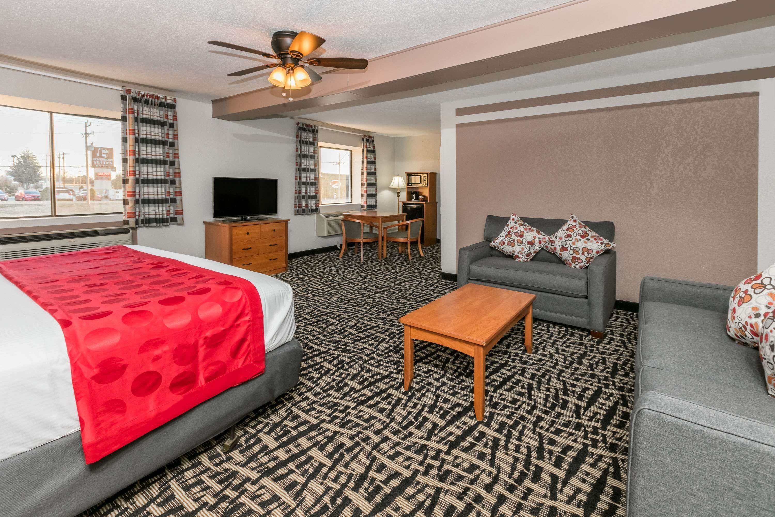 A hotel room with a bed, a sofa, a coffee table, a TV, a desk, and a ceiling fan.