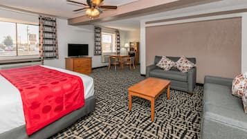 A hotel room with a bed, a sofa, a coffee table, a TV, a desk, and a ceiling fan.