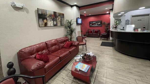 Un área de recepción con un sofá de cuero rojo, una mesa de centro con revistas, un televisor montado en la pared y un mostrador de recepción.