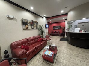 Ein Empfangsbereich mit einem roten Ledersofa, einem Couchtisch mit Zeitschriften, einem an der Wand befestigten Fernseher und einer Rezeption.