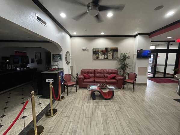 A lobby with a red leather sofa, a coffee machine, a trash bin, and a television on the wall.