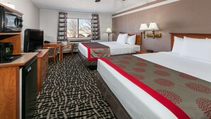 Habitación de hotel con una cama, dos mesitas de noche con lámparas, un escritorio con televisor, un ventilador de techo y una ventana con cortinas.