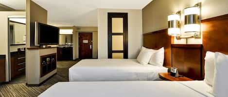A hotel room with two beds, a TV, a minibar, and a bathroom visible through an open door.