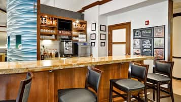 A bar area with a counter, bar stools, a coffee machine, and shelves with bottles and glasses.