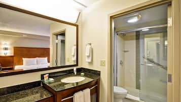 A hotel bathroom with a large mirror, a sink, a toilet, and a glass-enclosed shower.