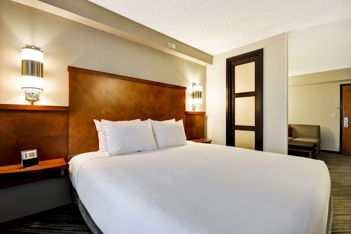 Habitación de hotel con una cama grande, cabecero de madera, lámparas de noche, un reloj y una silla.
