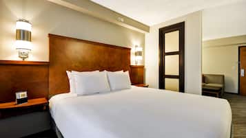A hotel room with a large bed, wooden headboard, bedside lamps, a clock, and a chair.