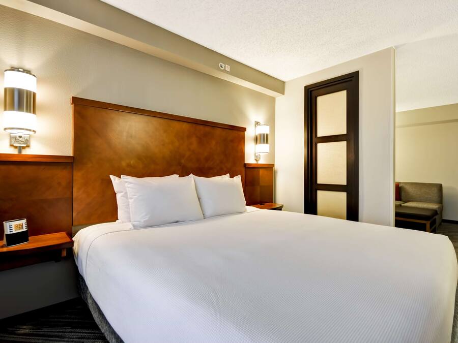 A hotel room with a large bed, wooden headboard, bedside lamps, a clock, and a chair.