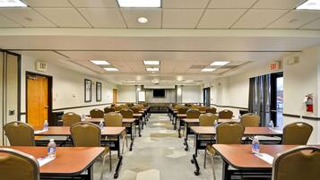 A conference room with multiple tables and chairs, equipped with water bottles, and exit signs on the walls.