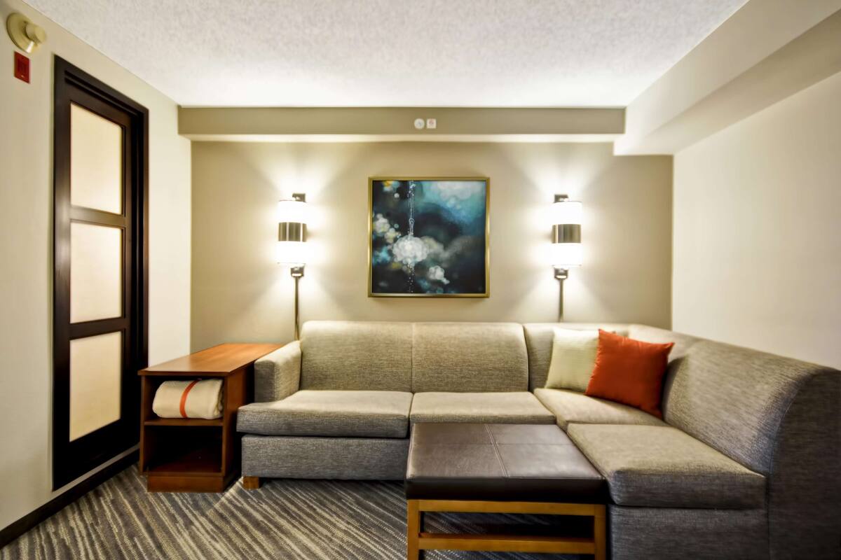 Una habitación de hotel moderna con un sofá modular, una pequeña mesa de madera y un cuadro en la pared.
