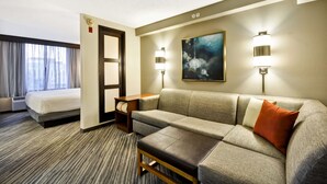 A hotel room with a bed, a sofa, a small table, a painting, and two wall-mounted lights.