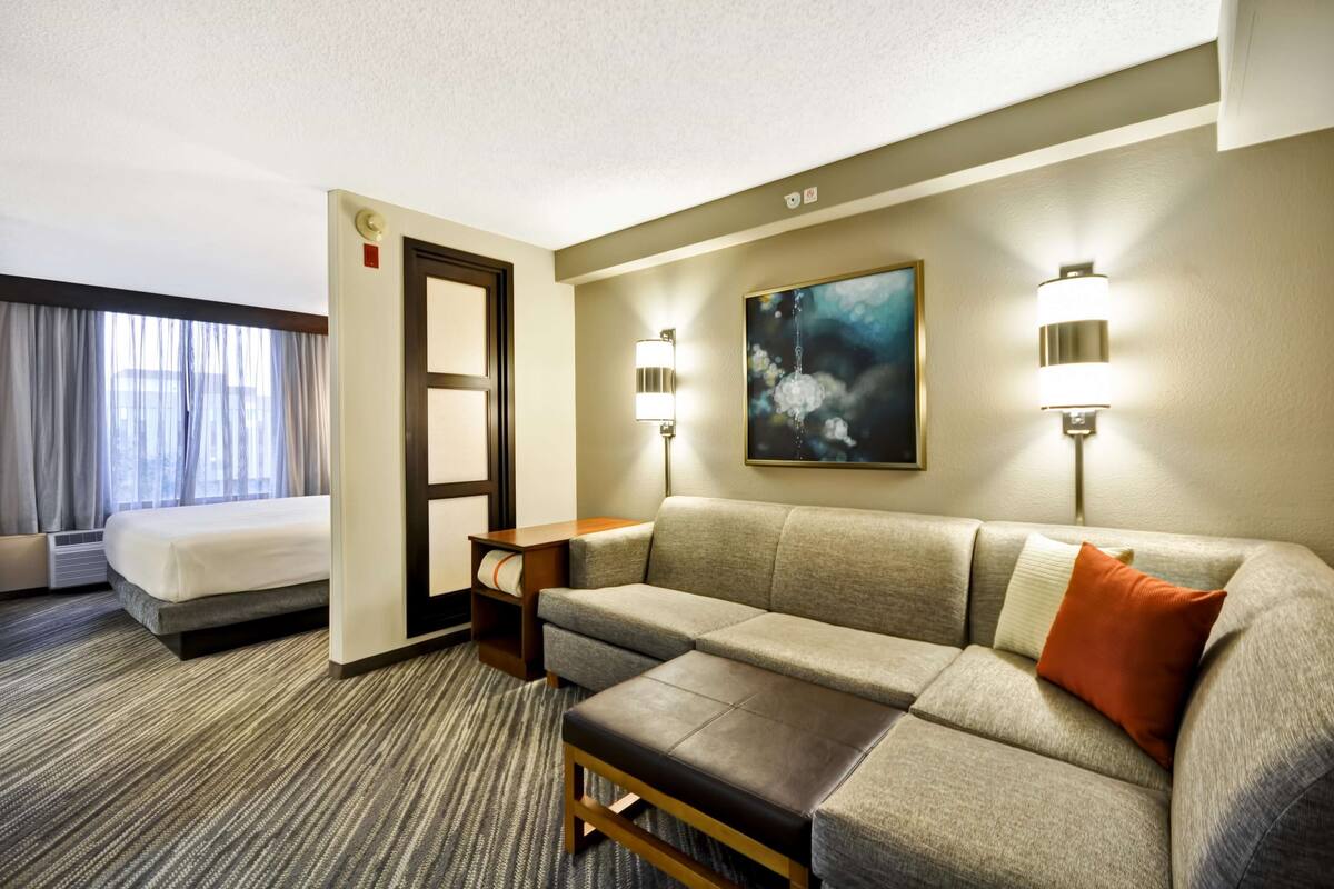 Habitación de hotel con cama, sofá, una mesita, un cuadro y dos lámparas de pared.