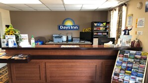 Een receptiebalie bij Days Inn, met een blauw en geel logo, een computer, printer en een plank met snacks.