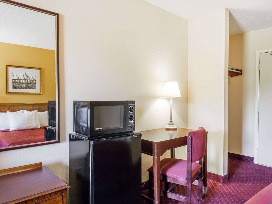 Une chambre d’hôtel de taille réduite, comprenant un lit, un petit bureau avec un micro-ondes, une chaise et une lampe.