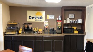 Een ontbijtbalk met een bordje met de tekst 'Daybreak Breakfast', een koffieapparaat, een magnetron en diverse bakken met eten.