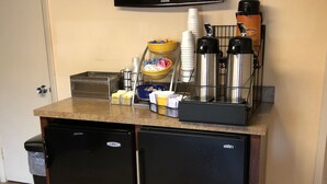 Een kitchenette met een koelkast, een koffiezetapparaat en een aan de muur bevestigde televisie.